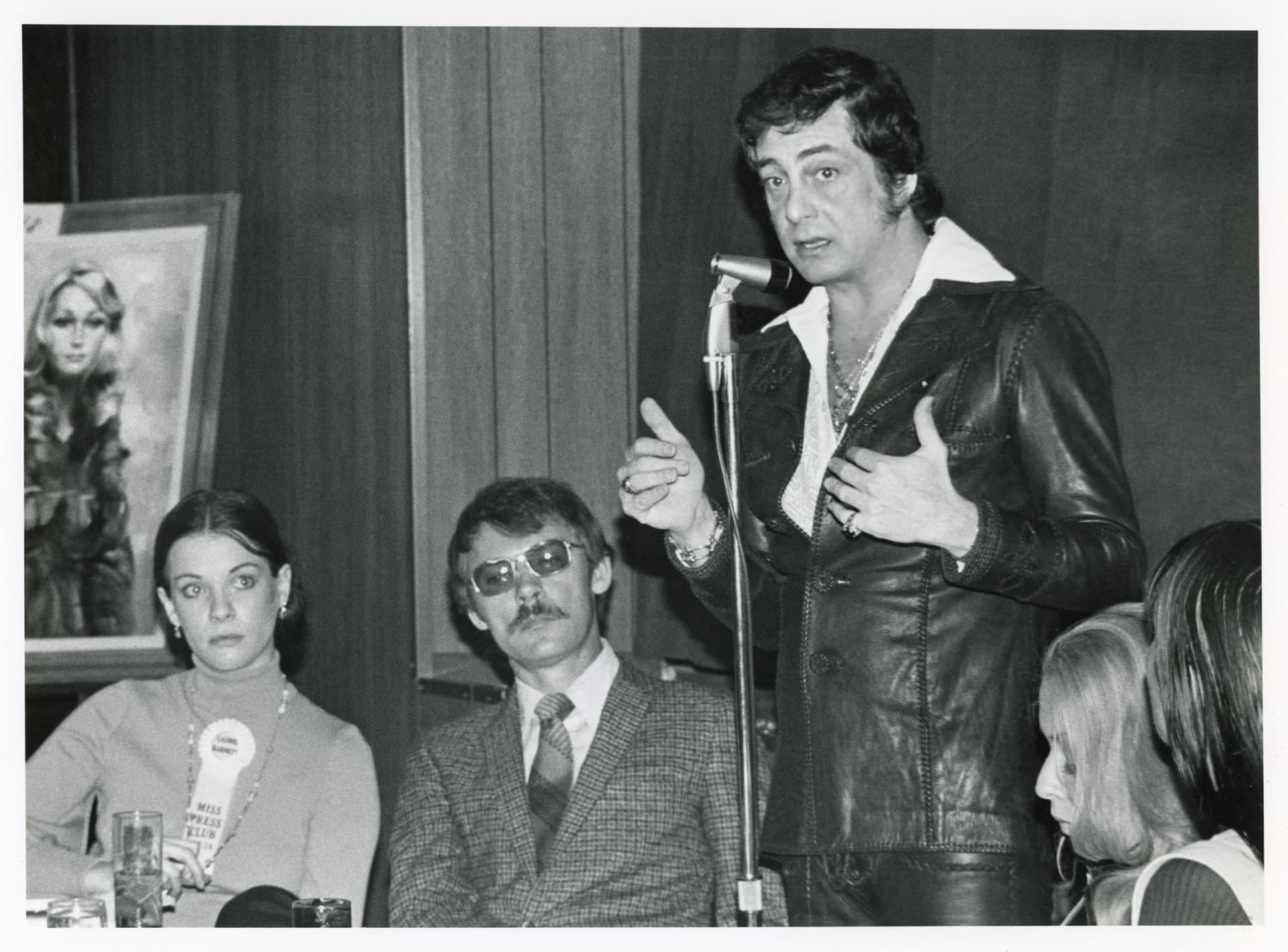 A man speaks at a podium while seated individuals listen.
